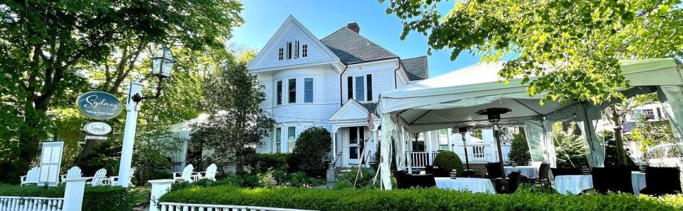 Exterior of L'etoile White house with a white Pickett fence surrounded by some green trees